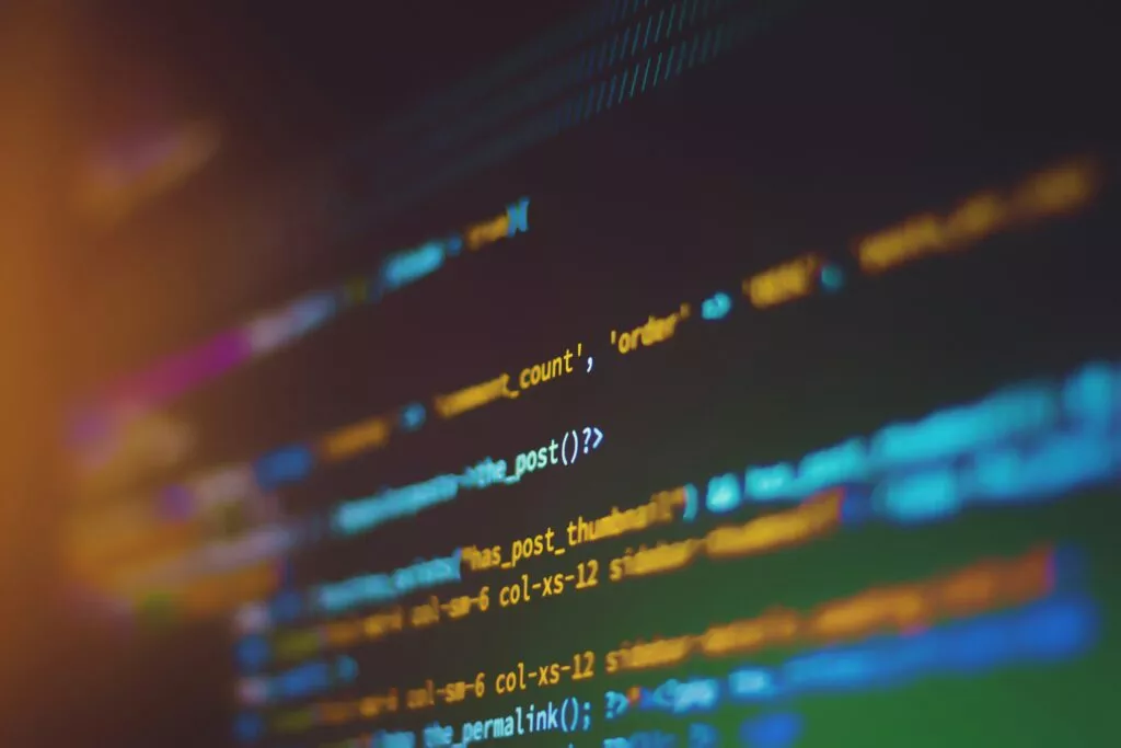 Unscharfe Darstellung von Programmcode auf einem Bildschirm mit blau-gelben Farbakzenten als Symbol für künstliche Intelligenz, Datenverarbeitung und digitale Technologien.