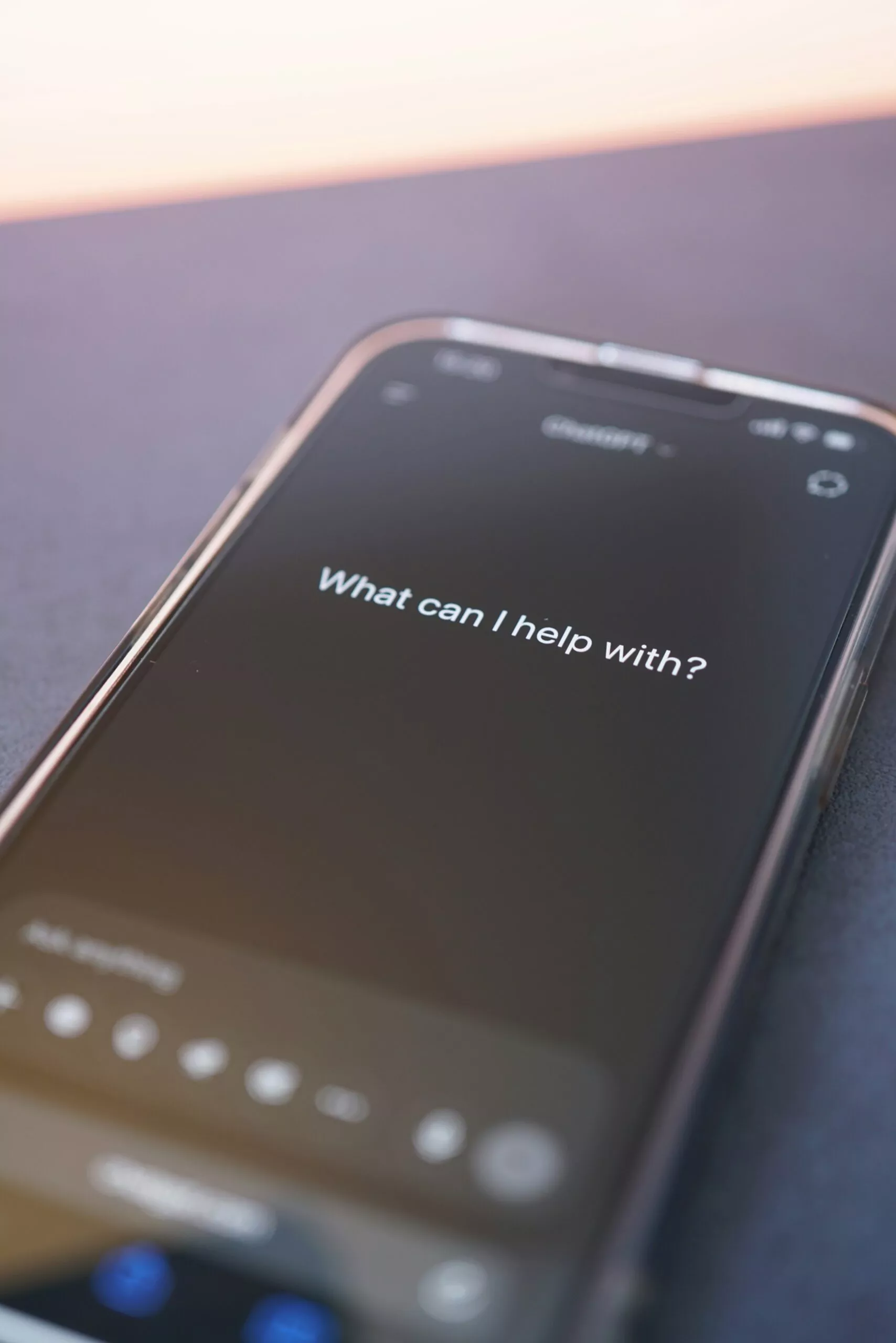 Smartphone mit aktiviertem Sprachassistenten oder KI-Chat. Auf dem Bildschirm ist die Frage „What can I help with?“ zu sehen.